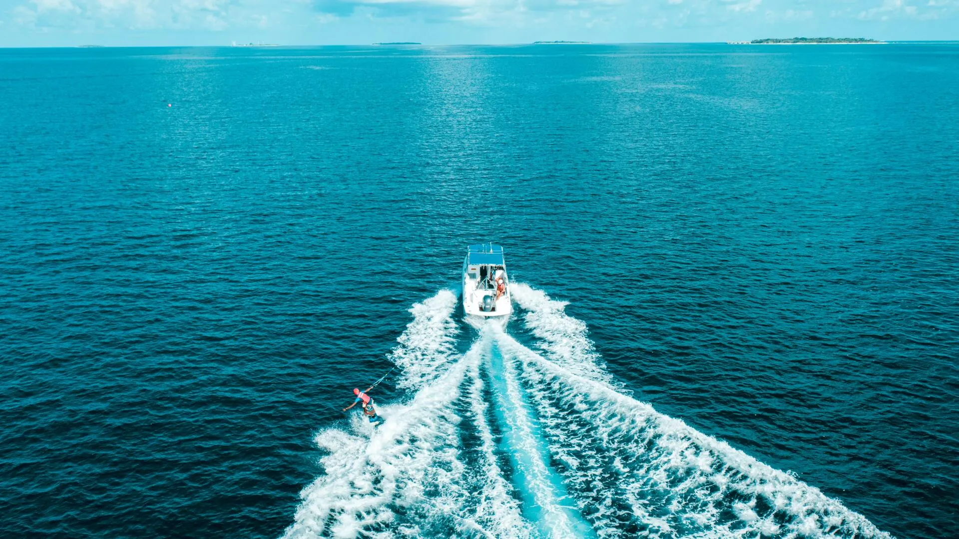 A motorboat cutting across open blue water while towing a wakeboarder.
