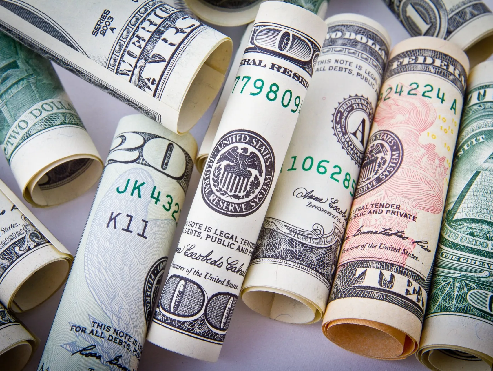 Rolled-up U.S. dollar bills of various denominations lying on a light surface.