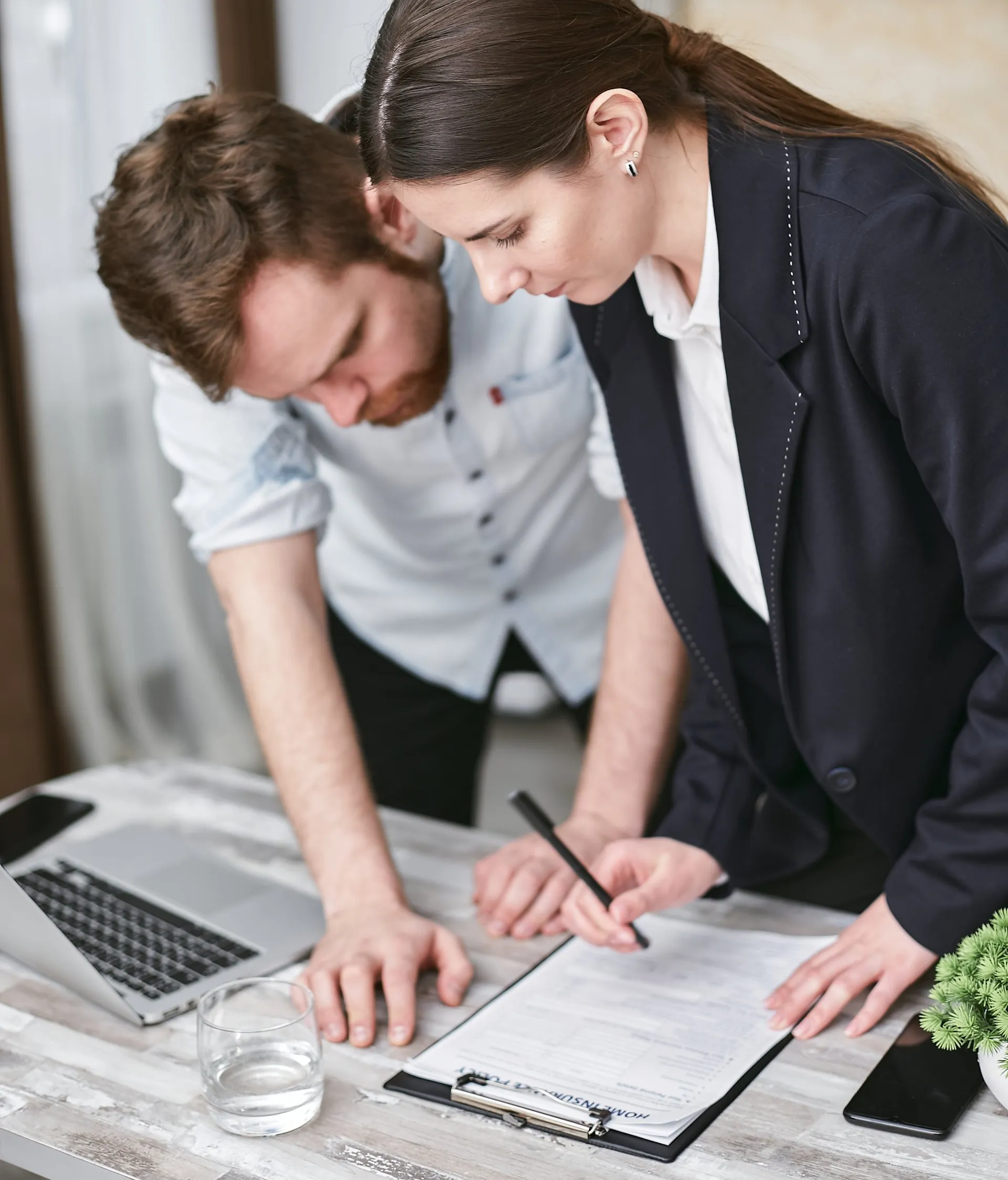 A woman in a suit helping a client review and sign an insurance policy document at a desk.