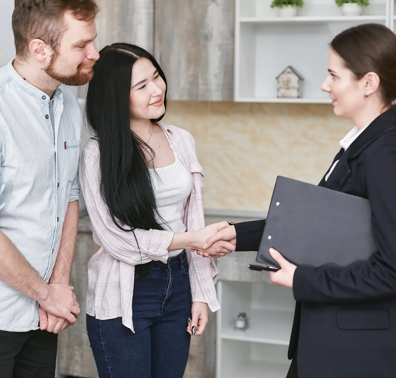A young couple shaking hands with an insurance agent holding a folder.