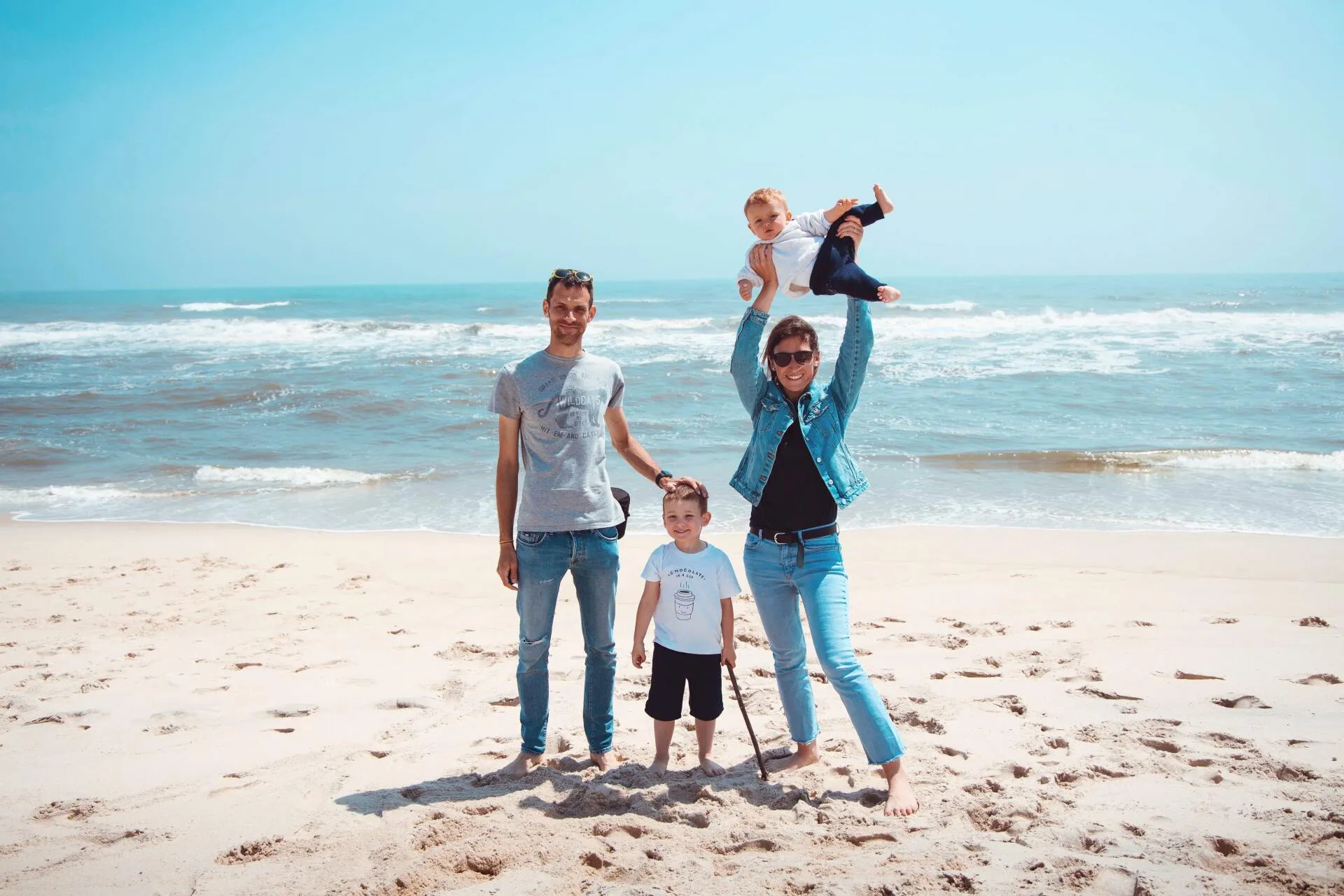Two parents and two young children enjoying a sunny day together at the beach.